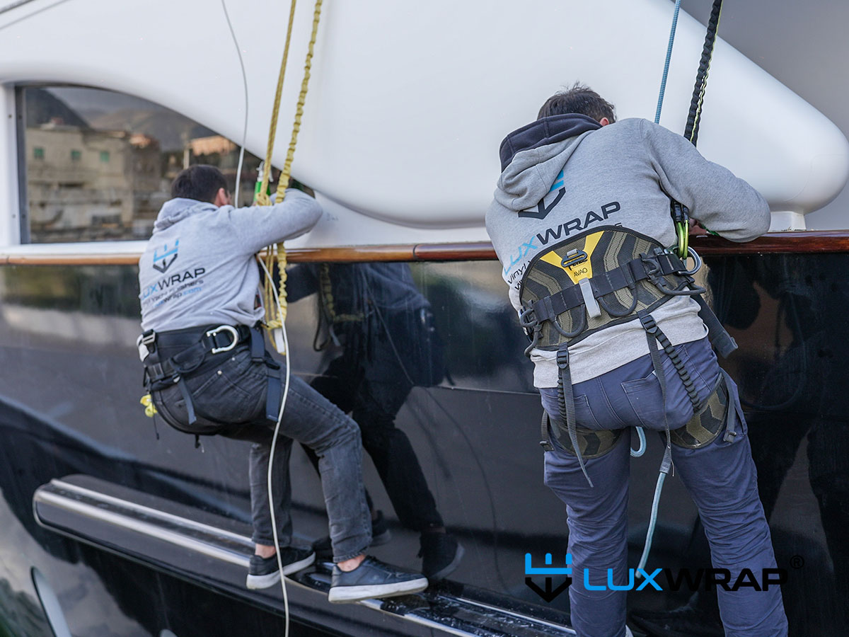 LuxWrap installer using a harness to access and wrap difficult-to-reach areas of a large superyacht hull