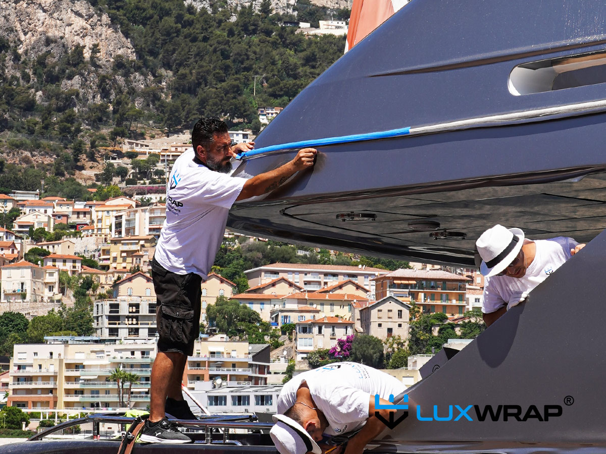 LuxWrap installer standing on a bulwark to wrap a large superyacht superstructure in metallic silver vinyl