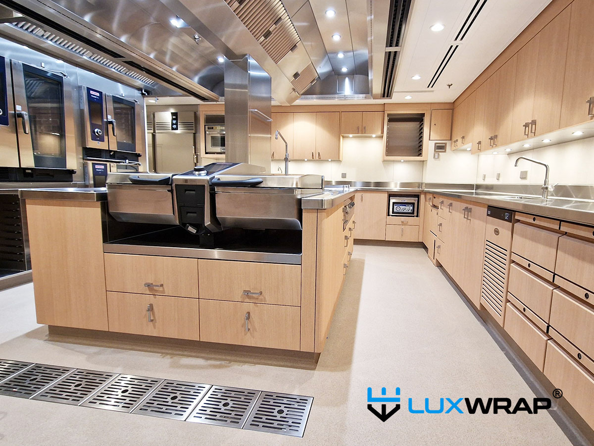 New-build mega yacht galley completely wrapped in wood grain architectural film — transforming a cold stainless steel space into a warm, welcoming environment