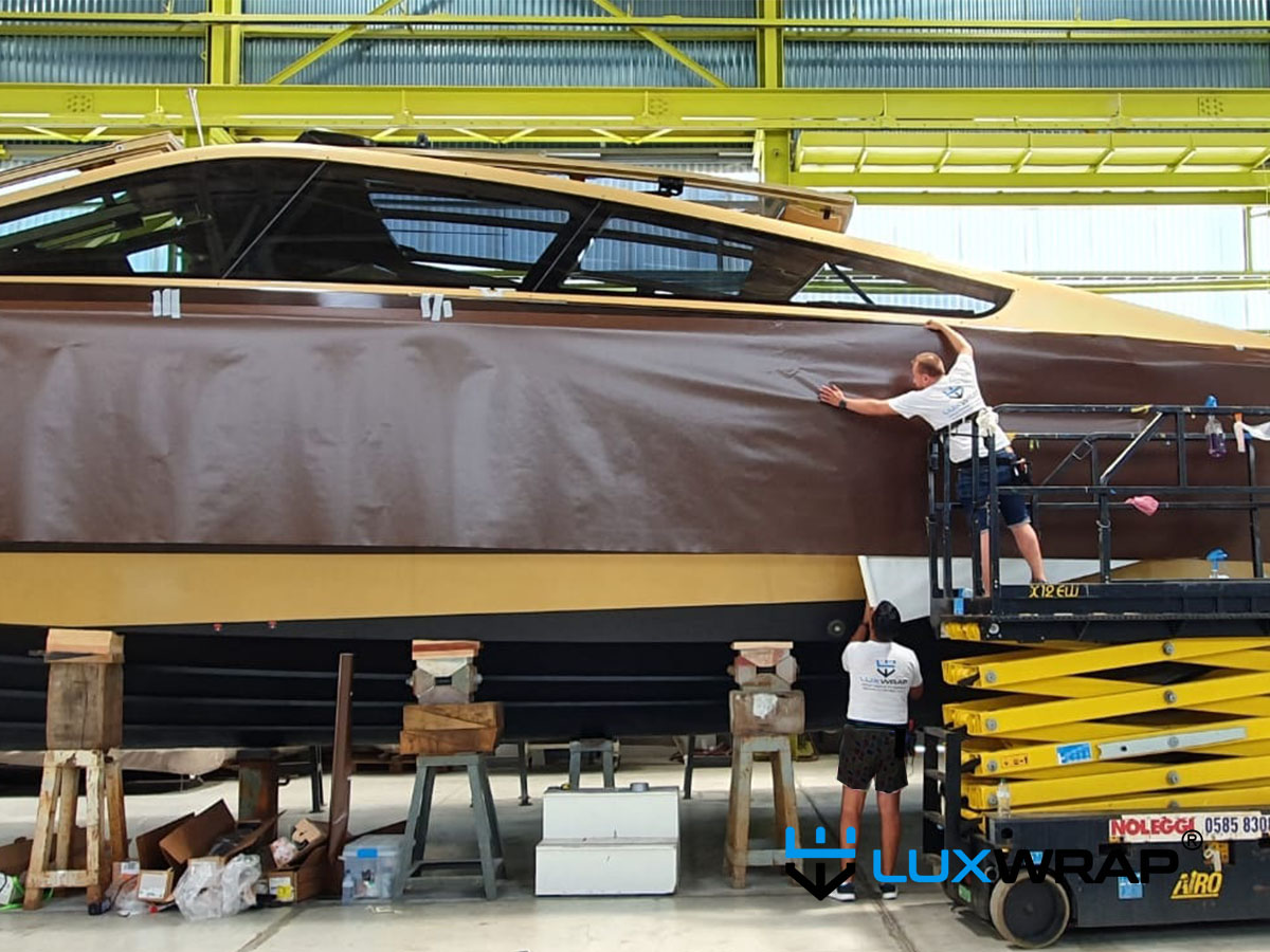 Custom-built GTB powerboat receiving a satin brown and gold colour-change wrap indoors using a scissor lift