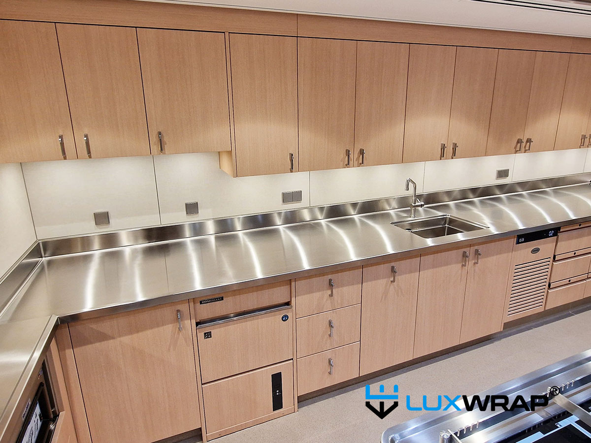 Stainless steel yacht galley wrapped with wood and textile architectural film finishes