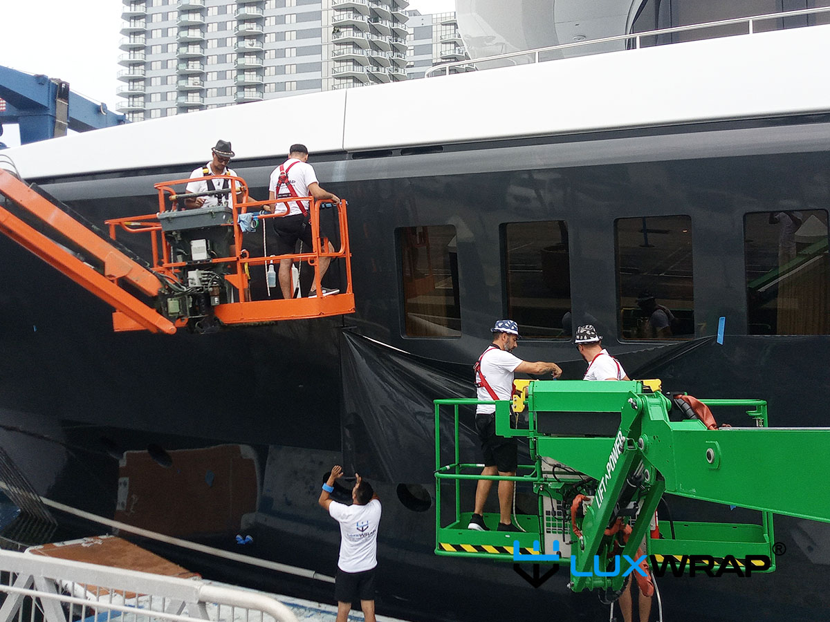 LuxWrap team wrapping a large superyacht hull using cherry pickers and floating rafts