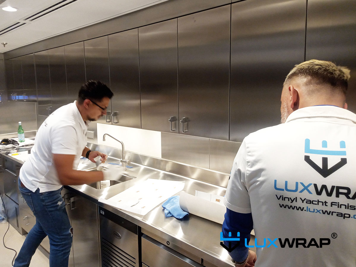 Large superyacht galley wrapped with wood grain architectural film — walls, doors, and drawers all covered for a complete transformation