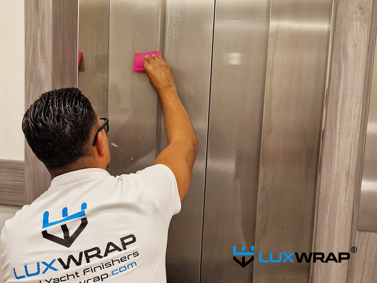 LuxWrap installer applying protective film to stainless steel panels inside a superyacht lift