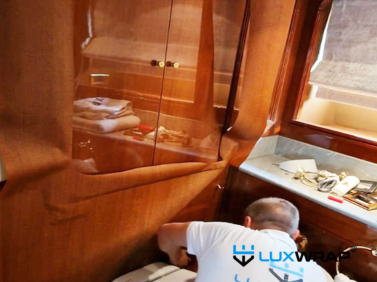 Superyacht gloss wood interior being refinished with colour-matched wood grain vinyl to replicate the original varnished finish