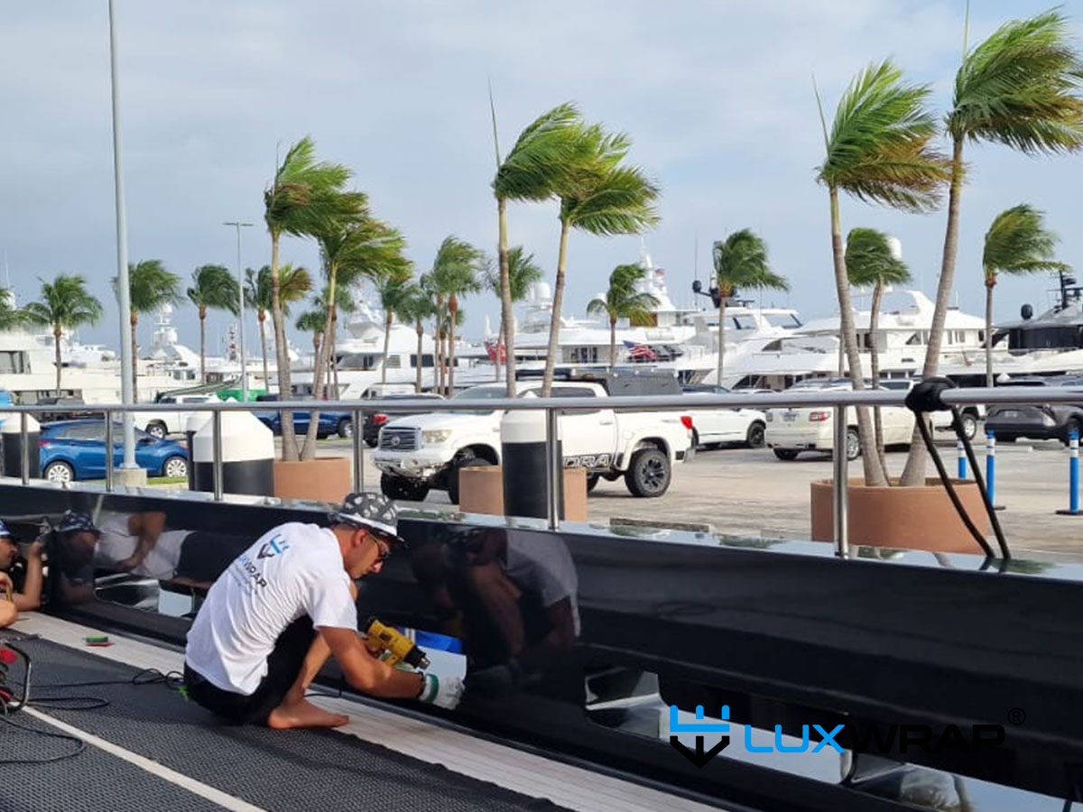 LuxWrap installer using harness and rope access to wrap a difficult section of a large superyacht hull